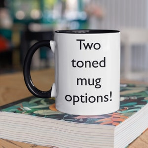 K&ouml;nnte beinhalten: Eine wei&szlig;e Keramiktasse mit schwarzem Henkel und schwarzem Rand. Auf der Tasse steht der Text "Two toned mug options!" gedruckt.
