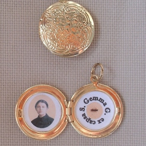 May include: Gold locket with an ornate design on the front and a photo of a woman and the text "Gemma G. & Caps" on the inside.
