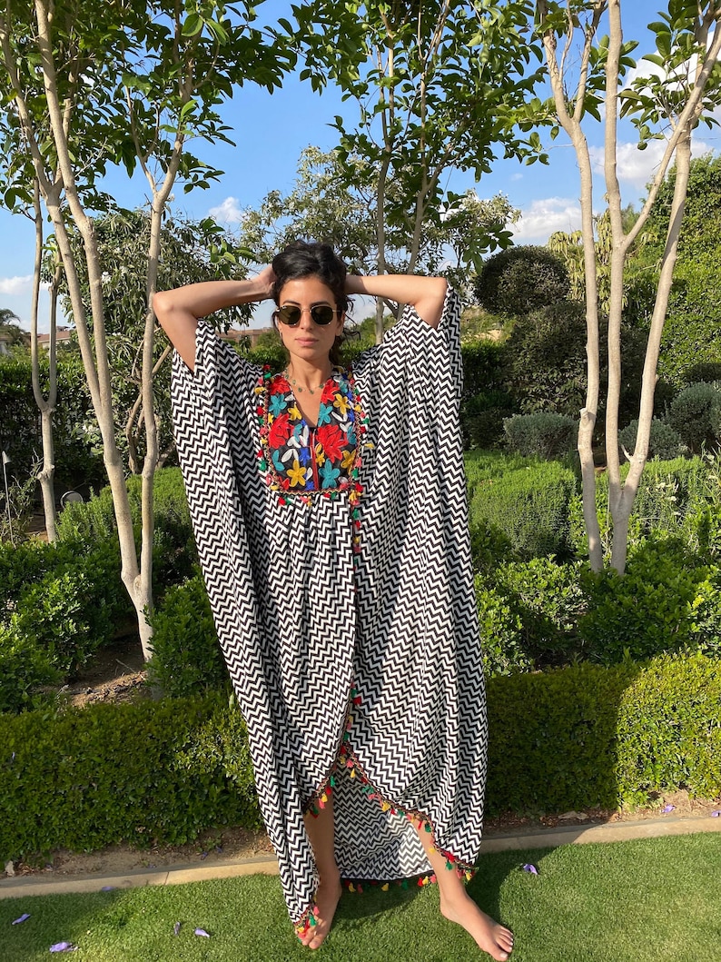 May include: A black and white chevron patterned kaftan with colorful embroidery and tassels. The kaftan has a long, flowing silhouette and is perfect for a summer day.