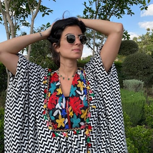 May include: A black and white chevron patterned kaftan with colorful embroidered flowers and tassels around the neckline.