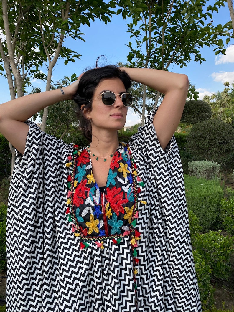 May include: A black and white chevron patterned kaftan with colorful embroidered flowers and tassels around the neckline.