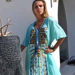 May include: A light blue, long-sleeved dress with colorful embroidery. The dress has a V-neck and a tassel hanging from the neckline.