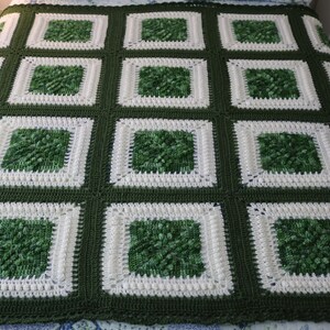May include: Handmade crochet blanket in a square pattern. The blanket features a repeating design of green squares with white borders, set against a dark green background. The squares have a textured, raised appearance.