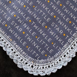 May include: A navy blue baby blanket with white text that reads "Twinkle Twinkle Little Star" and gold stars. The blanket has a white crocheted lace trim around the edges.