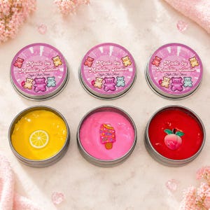 May include: Six small, round tins of colorful slime. The lids are pink with the text "Made by Maddie Studio" and bear illustrations. The slime colors are yellow with a lemon, pink with an ice cream, and red with a peach.