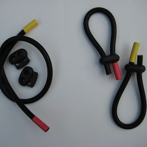 Op de afbeelding: Twee zwarte elastische koorden met gele en rode uiteinden. Een koord heeft twee zwarte plastic toggles.