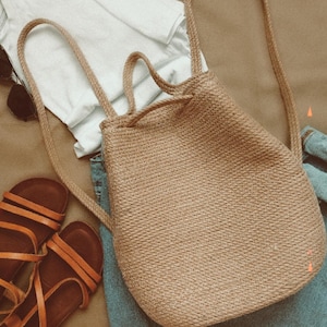 May include: A tan woven drawstring backpack with adjustable straps. The backpack is made of a natural material and has a casual, bohemian style.