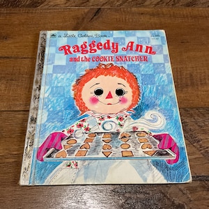 May include: A Little Golden Book featuring Raggedy Ann and the Cookie Snatcher. The cover shows Raggedy Ann holding a tray of cookies with a blue and white checkered background.