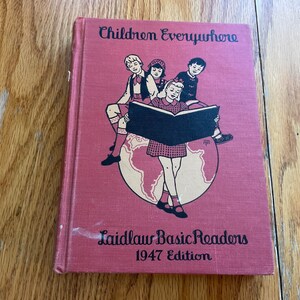May include: A vintage red book titled "Children Everywhere" with a black and white illustration of three children sitting on a globe. The book is part of the Laidlaw Basic Readers series and is the 1947 edition.