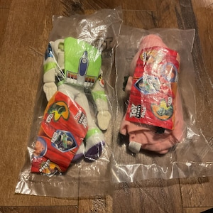 Może przedstawiać: Dwie pluszowe zabawki Toy Story Pals w oryginalnym opakowaniu. Pluszowa zabawka Buzz Lightyear jest zielona, biała i fioletowa. Pluszowa zabawka Rex jest r&oacute;żowa. Oba opakowania zawierają logo Toy Story Pals i postacie.