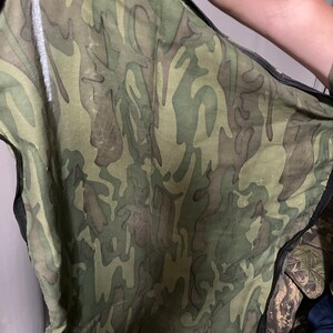 May include: A camouflage fabric with a zipper. The fabric is green, brown, and black.