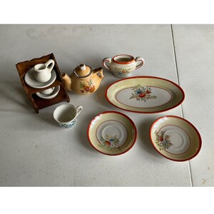 May include: A miniature tea set with a teapot, creamer, sugar bowl, and two cups and saucers. The set is decorated with floral patterns in shades of red, yellow, and blue on a white background. The teapot has a pineapple design.