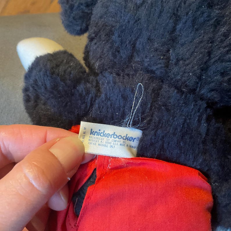 K&ouml;nnte beinhalten: Ein Pl&uuml;schtier mit schwarzem Fell, einem wei&szlig;en Fu&szlig; und einem roten Kleidungsst&uuml;ck. Ein Etikett mit dem Markennamen "knickerbocker" ist sichtbar. Das Spielzeug scheint Vintage oder Sammlerst&uuml;ck zu sein.