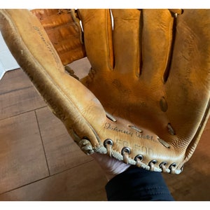 May include: A brown leather baseball glove with the name "Johnny Walker" written on it. The glove has a lace-up closure and is worn.