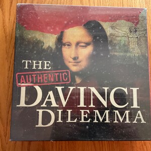 May include: The Authentic Da Vinci Dilemma board game box features a close-up of the Mona Lisa with a winking eye and a background image of a man in a Vitruvian Man pose.