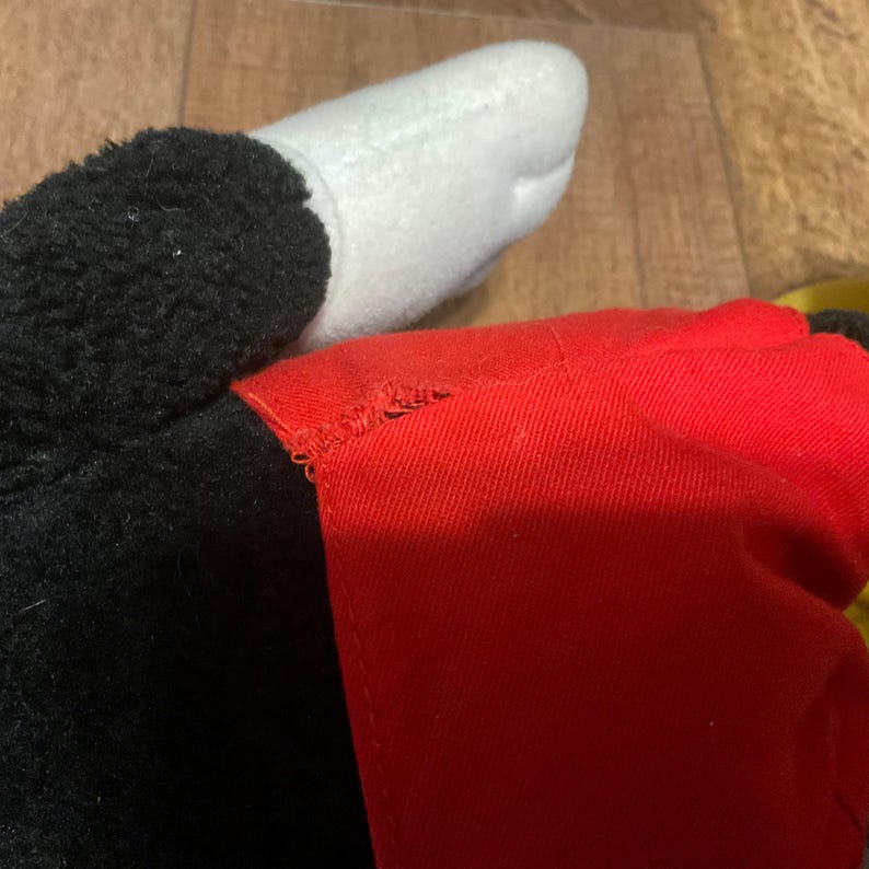 K&ouml;nnte beinhalten: Nahaufnahme eines Pl&uuml;schtiers mit wei&szlig;em Handschuh, schwarzem Fell und rotem Kleidungsst&uuml;ck. Das Spielzeugdesign umfasst einen wei&szlig;en Handschuh, schwarzes Fell und ein rotes Kleidungsst&uuml;ck, was auf eine Zeichentrickfigur hindeutet.