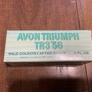 May include: A white box with green and blue text that reads "AVON TRIUMPH TR3'56 WILD COUNTRY AFTER SHAVE 2 FL. OZ. INGREDIENTS: S.D. ALCOHOL 40-B. WATER, GLYCERIN, FR"