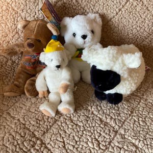 May include: Four plush toys: a brown bear, a white bear wearing a green and red hat, a white bear wearing a yellow hat, and a white sheep with a black face.
