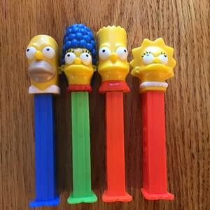 May include: Set of five Simpsons character themed Pez dispensers. The dispensers are yellow with blue, green, orange, and red bodies. The characters are Homer, Marge, Bart, Lisa, and Maggie.