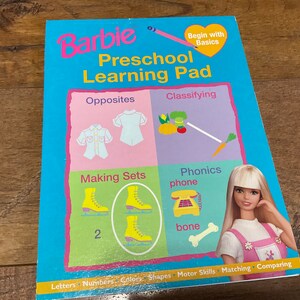 May include: A colorful Barbie Preschool Learning Pad with activities like opposites, classifying, making sets, phonics, and more. The pad features a cartoon image of Barbie and a heart with the text "Begin with Basics".
