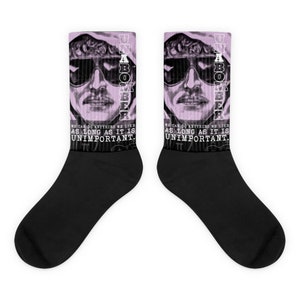 May include: A pair of black socks with a pink design featuring a man's face with sunglasses and the text "UNIBOMBER" and "WE CAN DO ANYTHING WE LIKE AS LONG AS IT IS UNIMPORTANT."