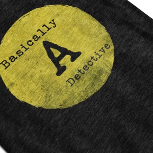May include: A yellow circle with the text "Basically A Detective" on a black t-shirt.