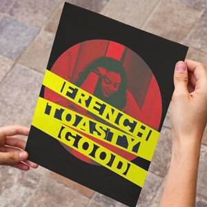 May include: A black poster with a red circle and yellow stripes. The poster features a photo of a person and the words "FRENCH TOASTY (GOOD)" in white block letters.