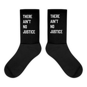 May include: A pair of black socks with white text that reads "THERE AIN'T NO JUSTICE".