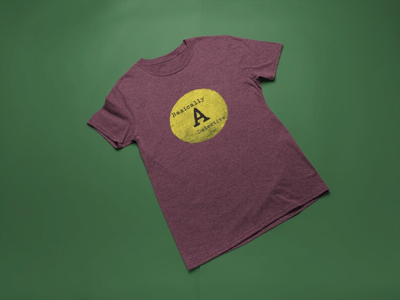 May include: A maroon t-shirt with a yellow circle and the text "Basically A Detective" inside the circle.