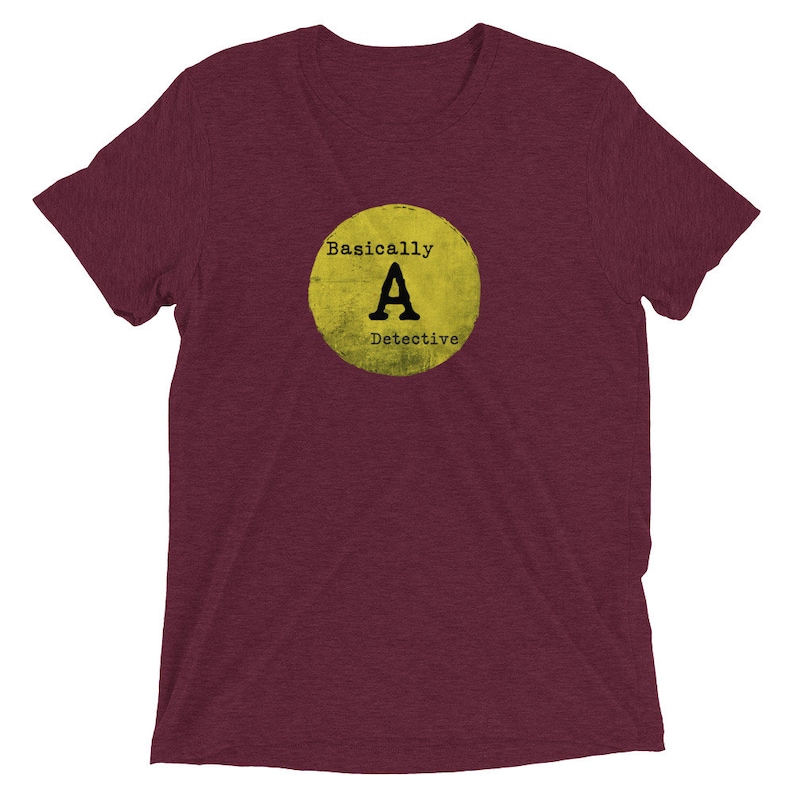 May include: A maroon t-shirt with a yellow circle graphic that says "Basically A Detective" in black text.