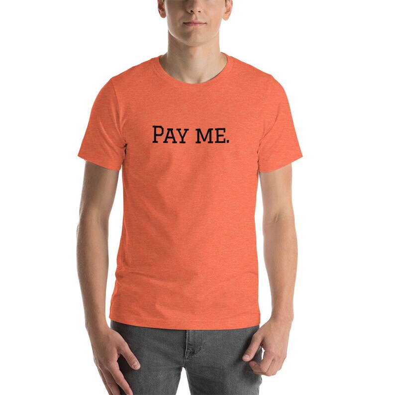 May include: Orange short-sleeve t-shirt with the text "PAY ME" printed in black. The shirt is made of a soft material and is suitable for casual wear. The t-shirt is a crew neck style.