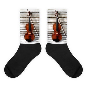 May include: A pair of black socks with a white background featuring a brown violin and bow on a wooden surface.