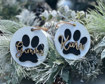 May include: Two white round ornaments with black paw prints and the names "Gemma" and "Kera" written in gold on them.
