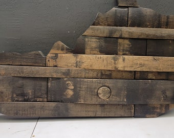 May include: A wooden wall art piece in the shape of the state of Kentucky. The art is constructed from reclaimed wood planks, showcasing varying shades of brown and dark char. A circular detail is visible.