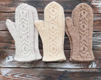 Könnte beinhalten: Drei gestrickte Fäustlinge in verschiedenen Beige- und Brauntönen werden gezeigt. Jeder Fäustling hat ein Zopfmuster. Die Fäustlinge sind nebeneinander angeordnet und zeigen ihre komplizierten Muster und Texturen.