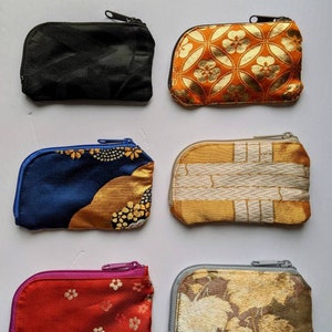 May include: Six small, zippered coin purses in various colors and patterns. The purses include a black, orange with gold floral design, navy blue with gold accents, gold and white striped, red with small gold flowers, and a gold floral pattern.
