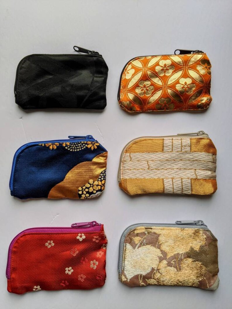 May include: Six small, zippered coin purses in various colors and patterns. The purses include a black, orange with gold floral design, navy blue with gold accents, gold and white striped, red with small gold flowers, and a gold floral pattern.