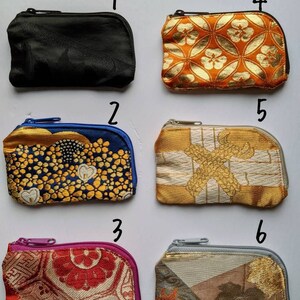 May include: A collection of six small, zippered coin purses. The purses feature various patterns and colors, including black, orange with gold floral designs, blue with gold embroidery, gold with white accents, red with floral patterns, and a mix of gray, gold, and brown.