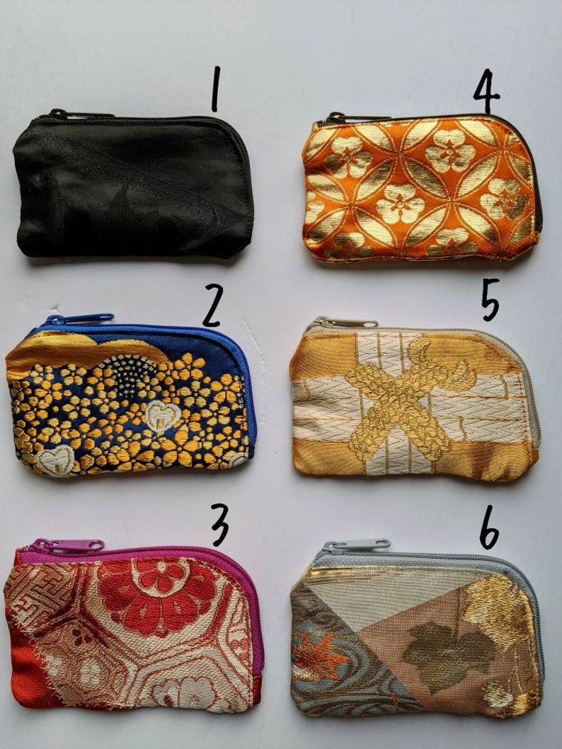 May include: A collection of six small, zippered coin purses. The purses feature various patterns and colors, including black, orange with gold floral designs, blue with gold embroidery, gold with white accents, red with floral patterns, and a mix of gray, gold, and brown.