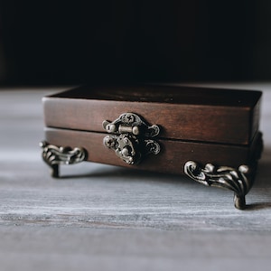 A small wooden box with a brown finish and ornate metal hinges and feet.