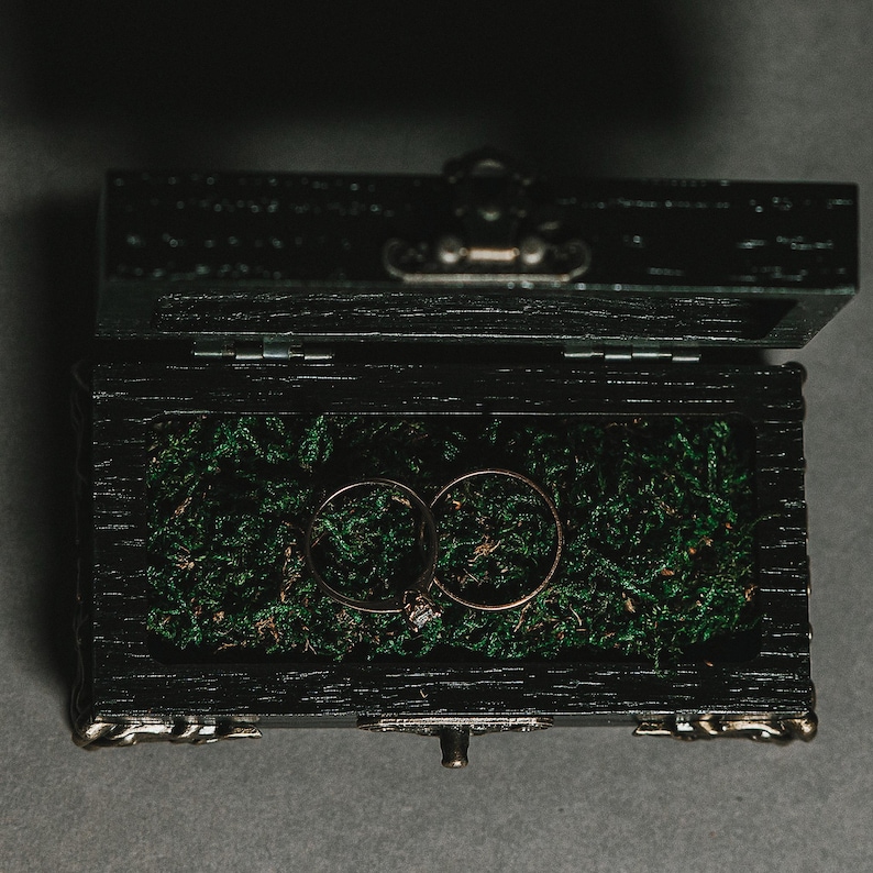 The box is adorned with  metallic hardware and sturdy metal legs, while the interior is cushioned with stabilized moss, offering a luxurious resting place for your rings.