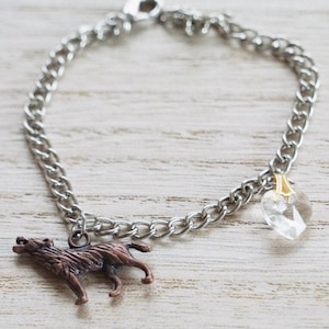 May include: A silver chain bracelet with a copper wolf charm and a clear crystal heart charm.