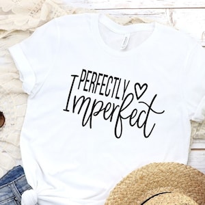 Puede incluir: Camiseta blanca con el texto "Perfectly Imperfect" en letras negras con un peque&ntilde;o s&iacute;mbolo de coraz&oacute;n.