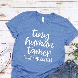 May include: A blue t-shirt with the text "tiny human tamer (just add coffee)" in white lettering.