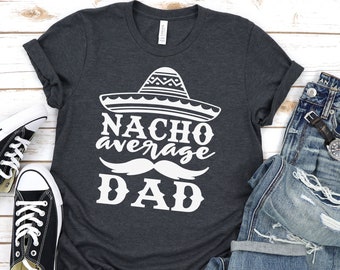 May include: A dark gray t-shirt with a white graphic that says "Nacho Average Dad" with a sombrero and a mustache.