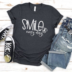 May include: A dark heather grey t-shirt with the text "SMILE every day" in white lettering and a small white four-leaf clover graphic.