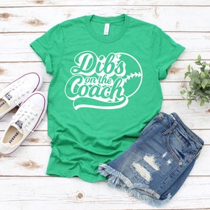 May include: Green t-shirt with white text that says "Dibs on the Coach" and a white baseball graphic.