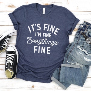 May include: A navy blue t-shirt with the text "It's Fine I'm Fine Everything's Fine" in white lettering.