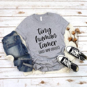 May include: A gray t-shirt with the text "tiny human tamer (just add coffee)" in black lettering.