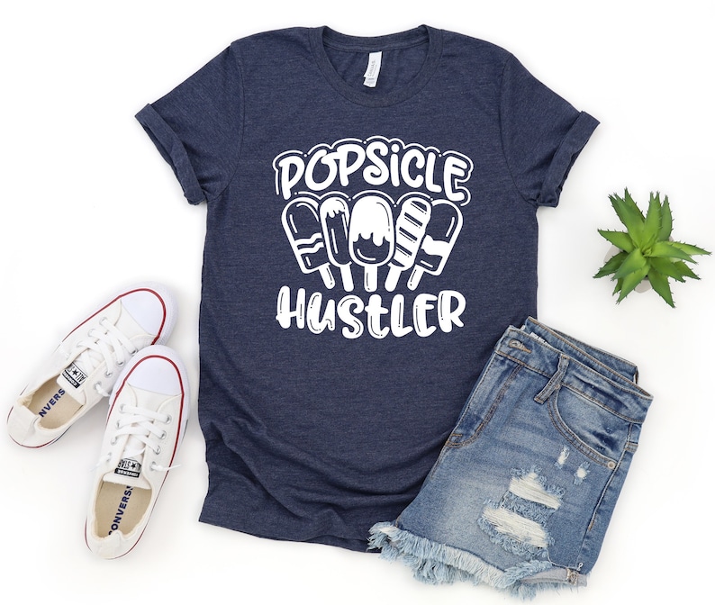 May include: A navy blue t-shirt with white text that reads "Popsicle Hustler". The text is surrounded by a graphic of four popsicles.